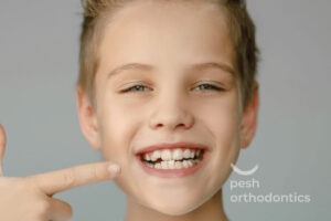 A child pointing at their teeth, illustrating early signs that may indicate the need for braces.