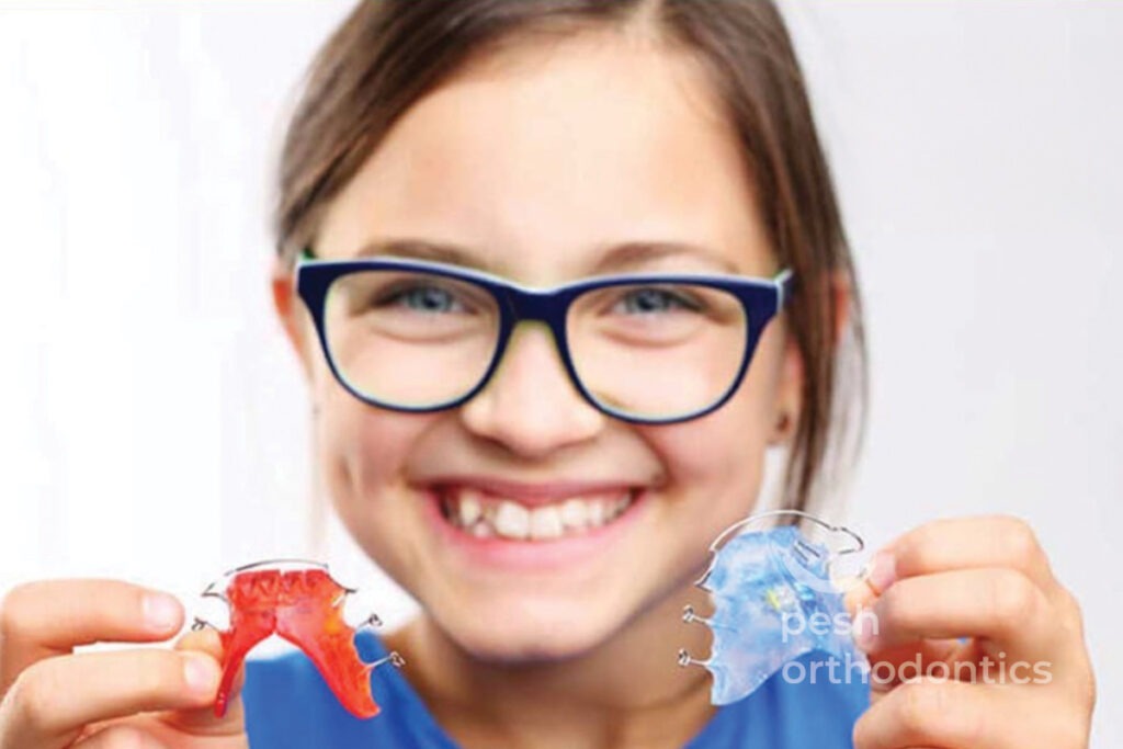 Teenager holding a retainer in both hands, smiling confidently.