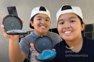 Two pre-teens smile while holding up clear aligners in a bright orthodontic office at Pesh Orthodontics in Menifee and Murrieta, CA.