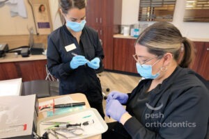 Two orthodontic assistants at Pesh Orthodontics preparing orthodontic tools and wires while wearing masks and gloves.